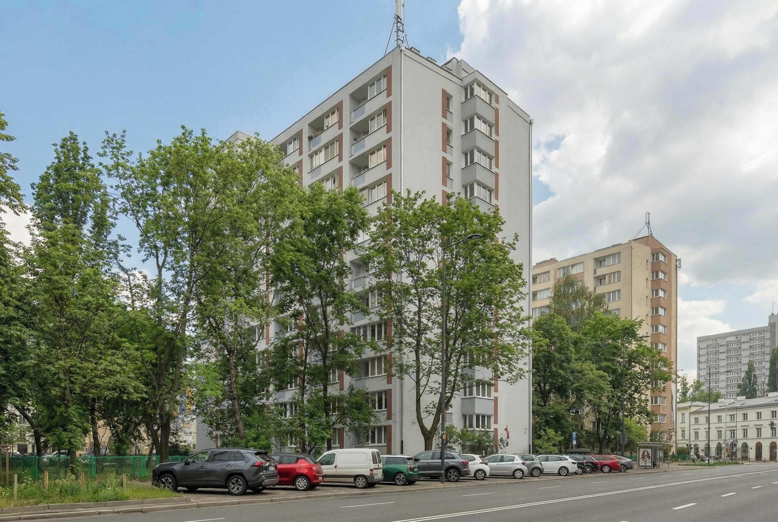 Un edificio residencial de varios pisos con balcones, rodeado de árboles y coches aparcados.