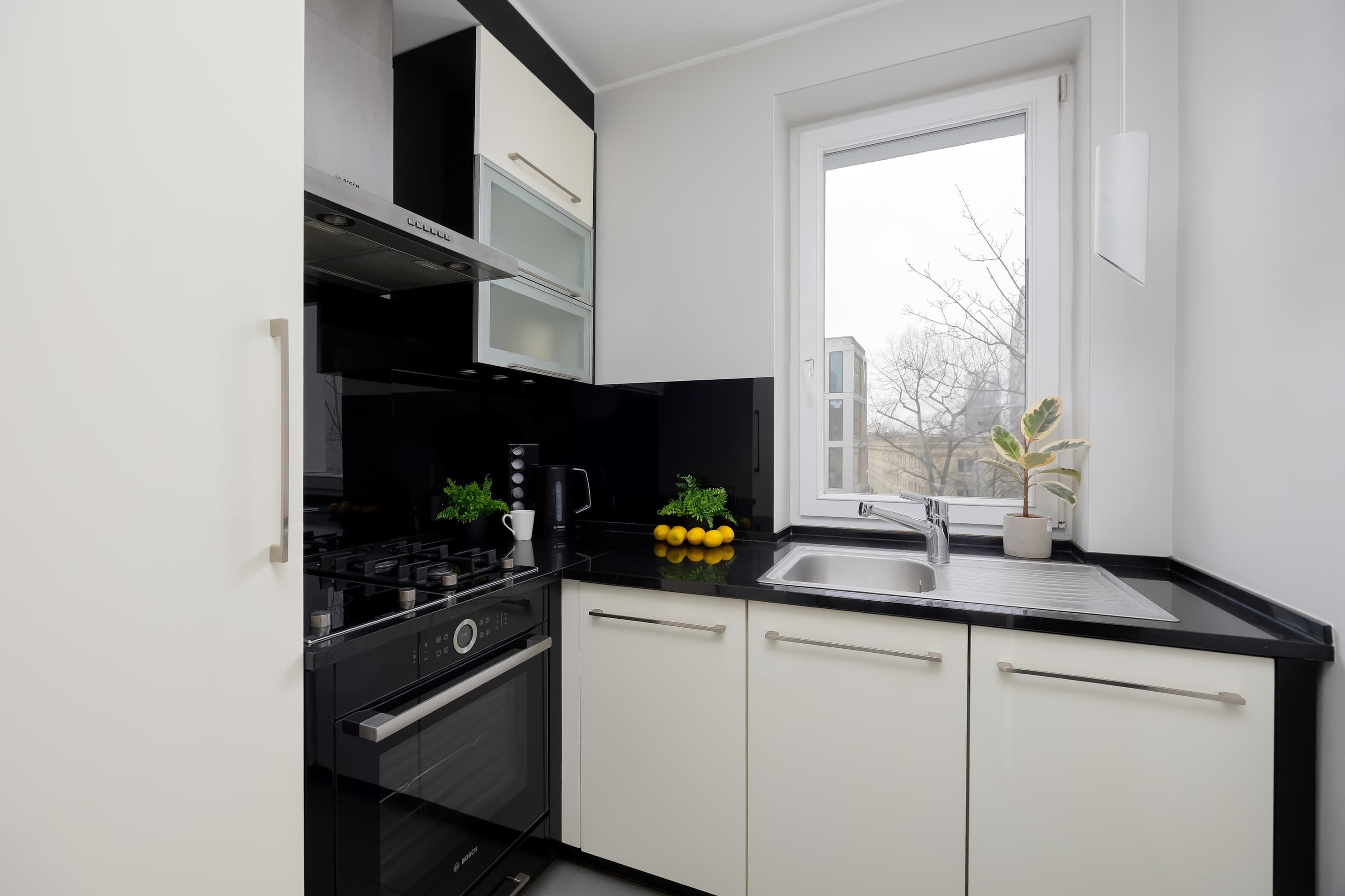 Eine moderne Küche mit weißen Schränken, einer schwarzen Arbeitsplatte und einem Fenster mit Blick auf Gebäude.