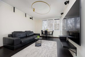 Ein modernes Wohnzimmer mit einem schwarzen Ledersofa, einem runden Couchtisch und einem großen Flachbildfernseher an der Wand.