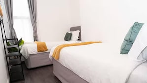 A hotel room with two beds, a wooden floor, and a window with curtains. - Near Transport - Parking - Wifi - Sleeps 3 (Newcastle-upon-Tyne)