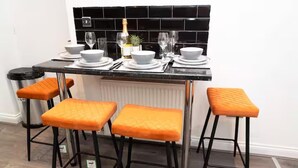 A kitchen with a black tiled backsplash, a countertop with white plates and glasses, and three orange cushioned stools. - Near Transport - Parking - Wifi - Sleeps 3 (Newcastle-upon-Tyne)