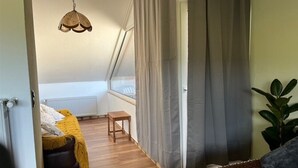Una habitación con techo inclinado, una pequeña mesa de madera, una manta amarilla y una planta.