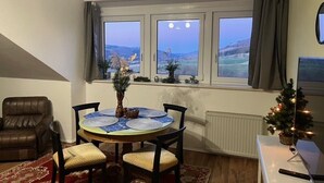 Un comedor con una mesa dispuesta para cuatro personas, una silla de cuero marrón, un pequeño árbol de Navidad y vistas al exterior a través de una ventana.