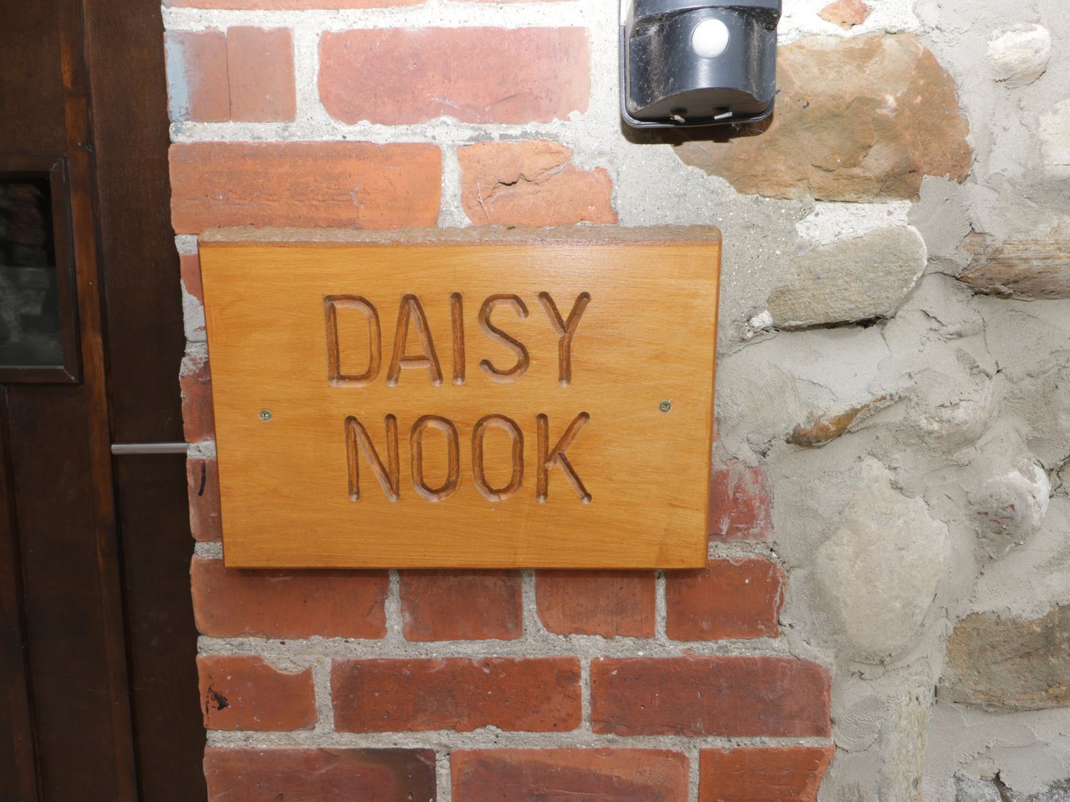 Un senyal de fusta amb el text 'DAISY NOOK' fixat en una paret de maó.
