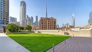 A rooftop garden with a green lawn, surrounded by modern buildings and a clear sky. - Vogue | Downtown near Dubai Mall | Burj Khalifa (Dubai)