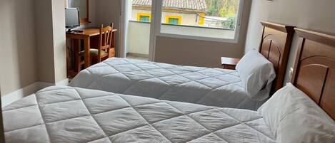 Une chambre avec deux lits, un bureau et une fenêtre donnant sur un bâtiment à l’extérieur.