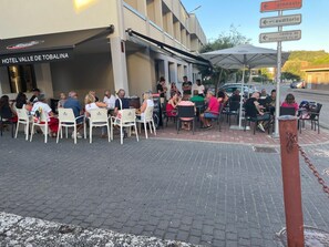 An outdoor seating area with tables and chairs, a building with a sign reading 'HOTEL VALLE DE TOBALINA', and directional signs for 'gimnasio' and 'auditorio'. - Hotel Rural Valle de Tobalina (Valle de Tobalina)