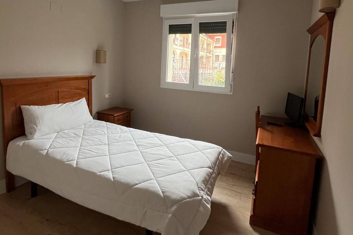 Ein Schlafzimmer mit Bett, Nachttisch, Kommode, Fenster und Lampe.