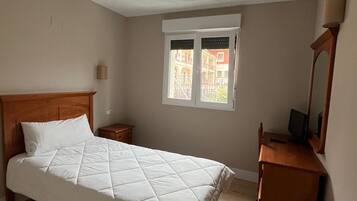 Un dormitorio con cama, mesita de noche, cómoda, ventana y lámpara.