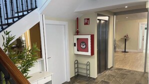 Un pasillo con una escalera, una puerta, un ascensor y una planta.