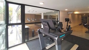 Een sportschool met trainingsapparatuur, grote ramen en uitzicht op de straat.