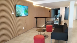Een modern interieur met een televisie aan een houten wand, een glazen balustrade, een trap en een zithoek met een bank en voetenbankje.