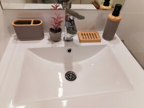 Ein Waschtisch mit einem modernen Wasserhahn, einer Topfpflanze, einem Seifenspender und einem Holztablett.