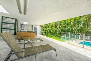 A modern outdoor living area with a pool, lounge chairs, and a kitchen area with a view of lush greenery. - Luxury Home w/pool in Bryanston (Sandton)