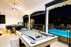 A pool table with billiard balls, a dining area with chairs, and a poolside view. - Villa Kynoa 4 stars (Saint-François)