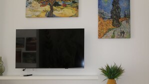A flat-screen TV mounted on a white wall, flanked by two paintings.