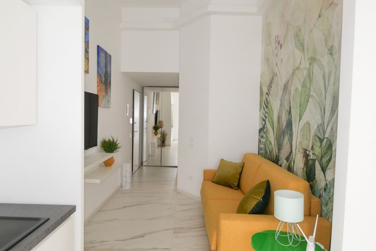 Una sala de estar moderna con un sofá, una mesa de centro y una lámpara fijada a la pared. Se ve un pasillo que conduce a otra habitación.