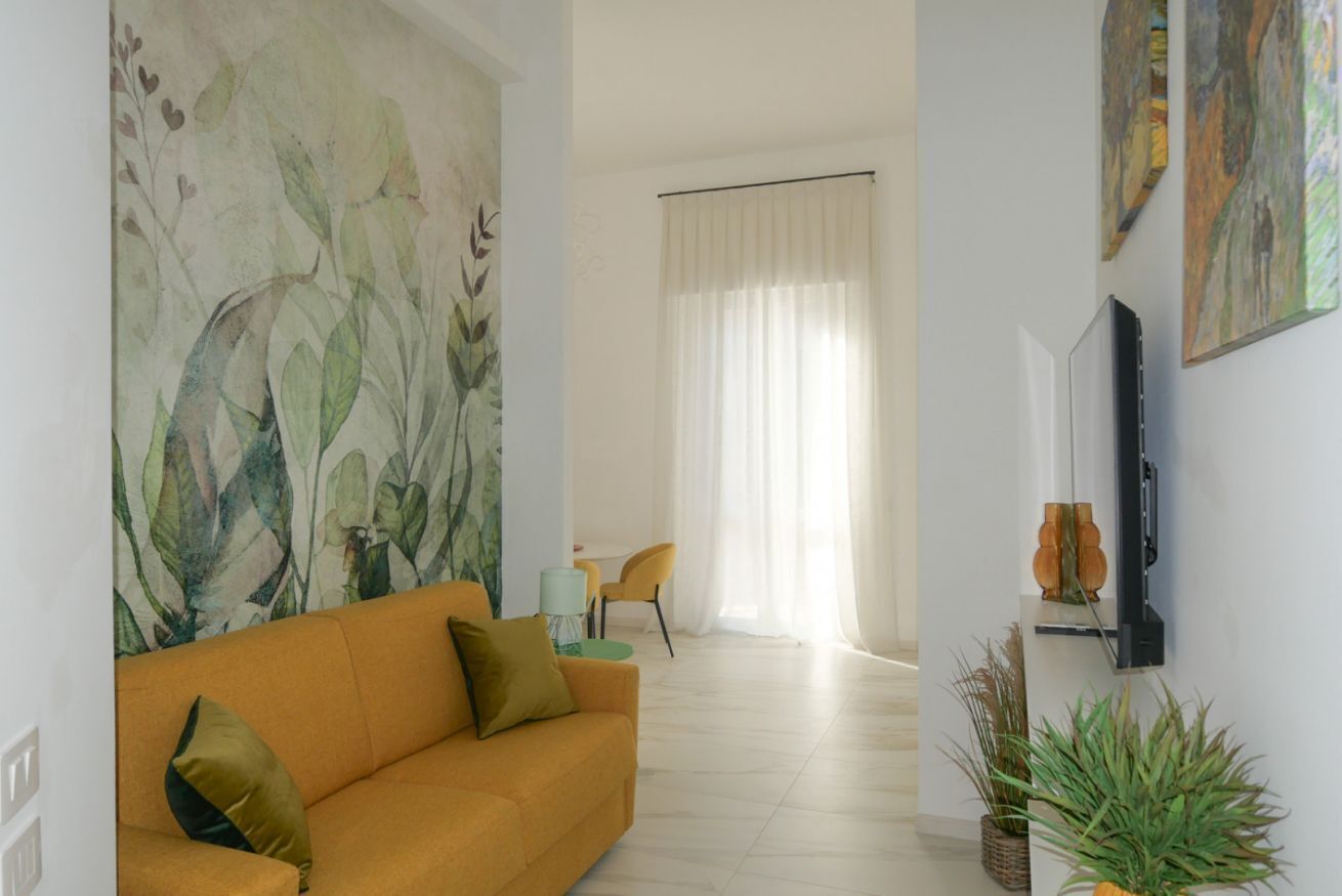 Ein Wohnzimmer mit einer Couch, einem Gemälde, einem Fernseher und einem Essbereich mit Stuhl und Tisch.
