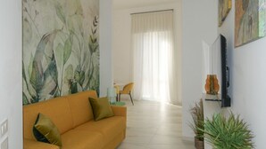 A living room with a sofa, a painting, a television, and a dining area with a chair and table.