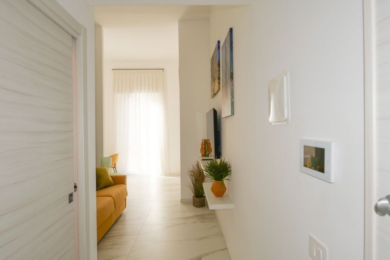 Un couloir avec un canapé jaune, une plante en pot et un téléviseur fixé au mur.