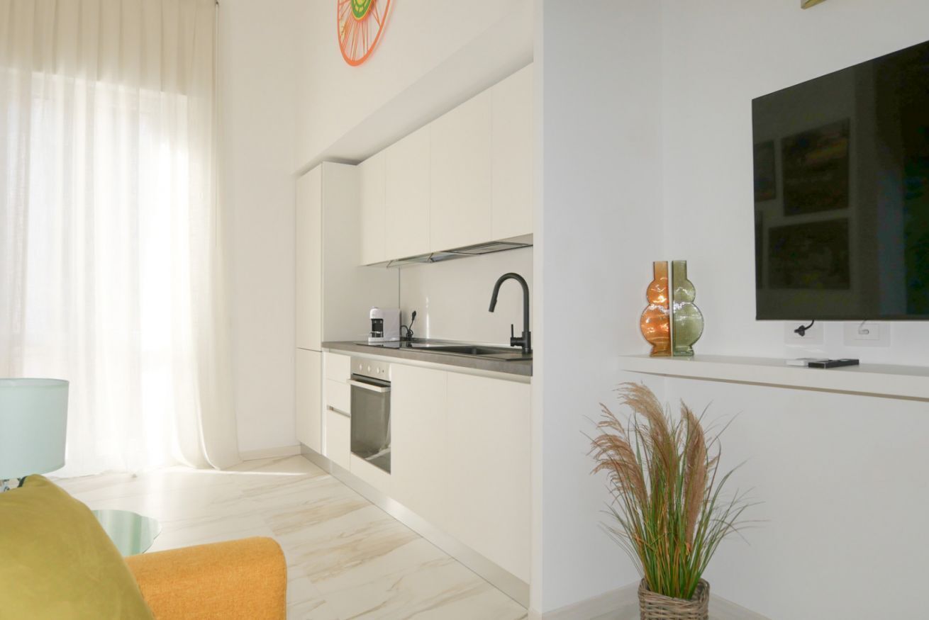A modern kitchen with white cabinets, a built-in oven, and a flat-screen TV mounted on the wall.