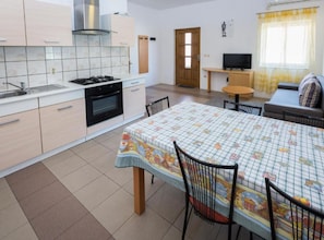 A compact kitchen with a gas stove, oven, and white cabinets. There's a dining table with chairs and a TV in the living area. - Mediterraneo Goga Apartments (Mali Losinj)