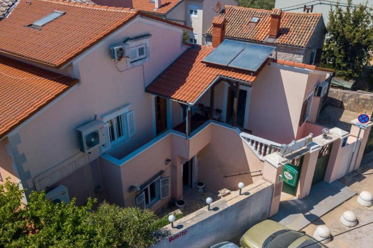 A multi-story residential building with a red-tiled roof, air conditioning units, and a small balcony.