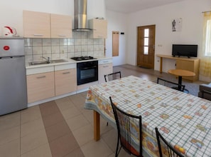 A compact kitchen with a stove, sink, and cabinets, a dining table with chairs, and a TV in a separate room. - Mediterraneo Goga Apartments (Mali Losinj)