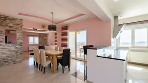A modern kitchen with a central island, a dining area with a table and chairs, and a view of the outdoors through large windows. - Villa Ana With Outdoor Pool, Sauna and Hot-tub (Kastela)