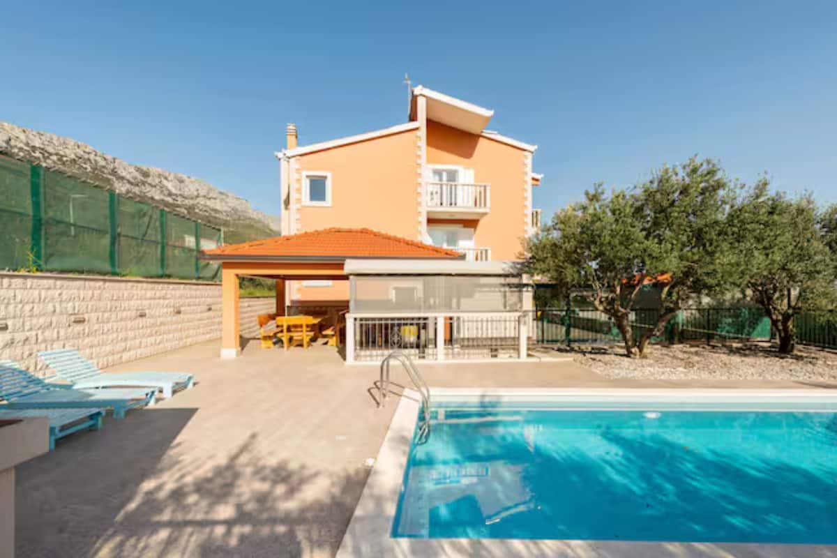A two-story building with a swimming pool, outdoor seating, and a fenced area.
