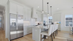 Una cocina moderna con armarios blancos, electrodomésticos de acero inoxidable y una isla central con taburetes de bar.