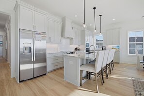 A modern kitchen with white cabinetry, stainless steel appliances, and a central island with bar stools. - For Whom The Beach Tolls: New Coastal Retreat w/ Pool & Stunning Views (Murrells Inlet)