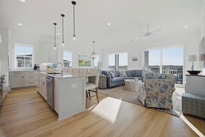 A spacious living area with a kitchen, a dining area, and a large window offering a view. - For Whom The Beach Tolls: New Coastal Retreat w/ Pool & Stunning Views (Murrells Inlet)