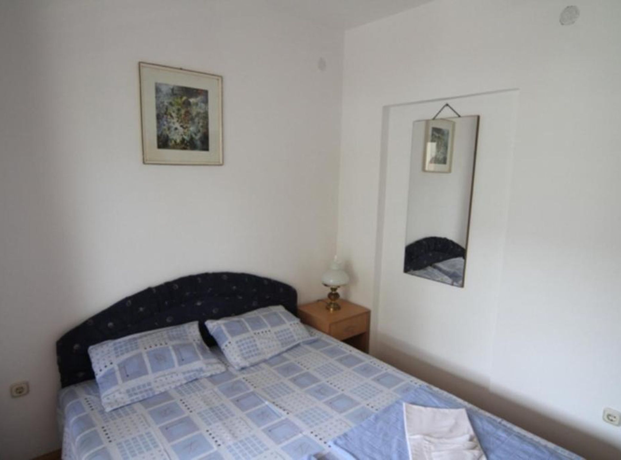 A bedroom with a bed, a nightstand, a lamp, a framed picture, and a mirror on the wall.