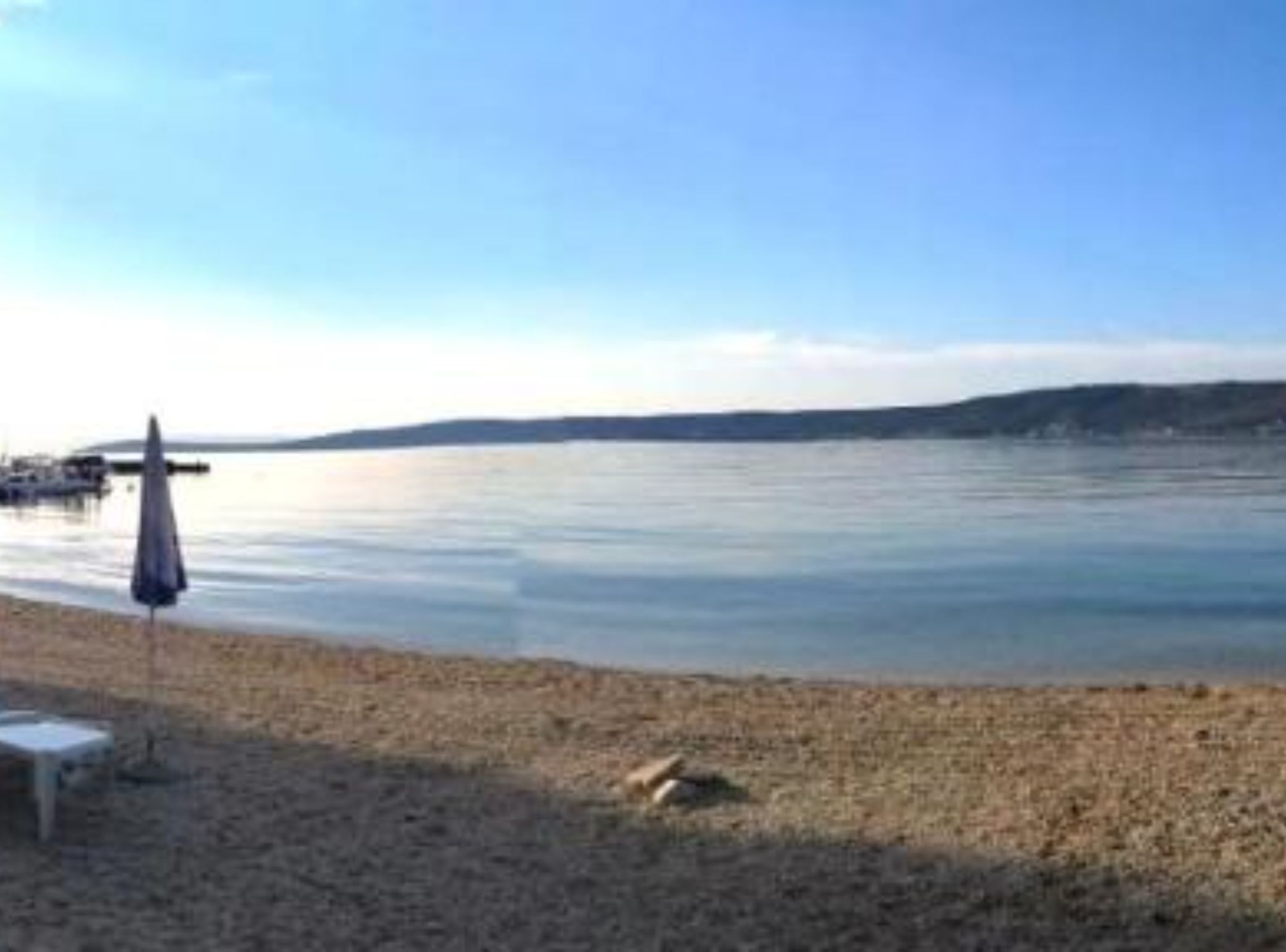 Une plage avec un ciel dégagé, une eau calme et une côte visible au loin.
