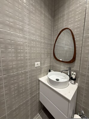 Ein Badezimmer mit grauen Fliesen, einem weißen Waschbecken und einem spiegel mit Holzrahmen.