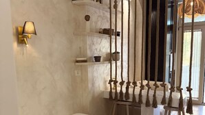 Ein modernes Schlafzimmer mit einem Bett, einem an der Wand befestigten Bücherregal, einer Lampe und einem Jutevorhang.