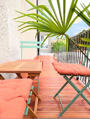 A balcony with wooden flooring, a green metal chair, a wooden table, and a large green plant. - Luvra 1 Dh rmi Spacious Balcony Hideaway (Himarë)