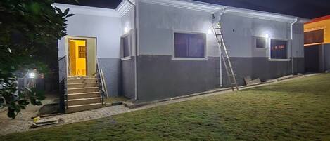 A two-story building with a visible staircase leading to the entrance, a ladder leaning against the wall, and a well-maintained lawn in front.