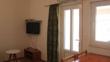 Una habitación con una mesa de comedor de madera, un televisor montado en la pared, un mueble de madera pequeño y un ventanal con cortina corredera.