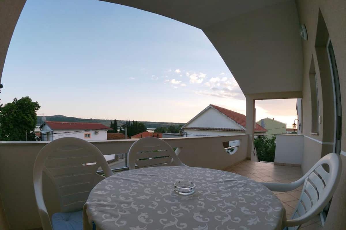 Uma varanda com uma mesa redonda e cadeiras, com vista para uma área residencial com casas e um céu claro.