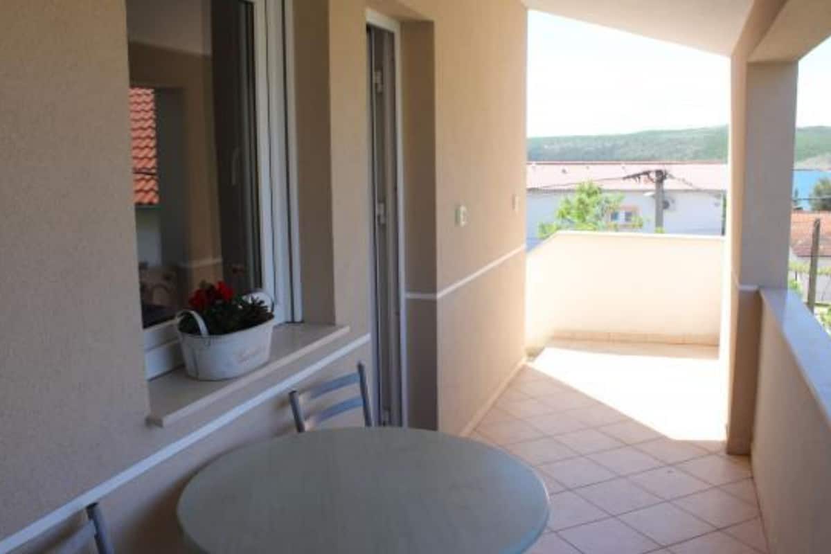 Uma varanda com mesa e cadeiras, uma janela com uma planta e vista para edifícios e colinas.