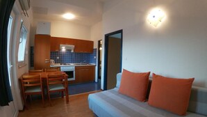 A compact living space with a kitchenette, a dining area, and a sofa with orange cushions. - Sanja Apartments Posedarje (Posedarje)