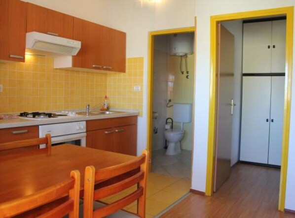 Cocina compacta con armarios de madera, una mesa de comedor y un baño pequeño con inodoro y lavabo.