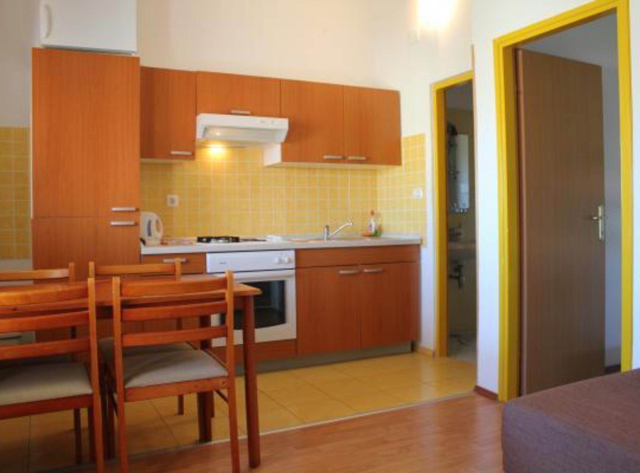Une cuisine de taille réduite, dotée de meubles en bois, d’une cuisinière et d’un évier. On y trouve également une table à manger avec des chaises.