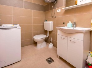 Pieni kylpyhuone, jossa on wc, pesuallas ja pieni pesukone.
