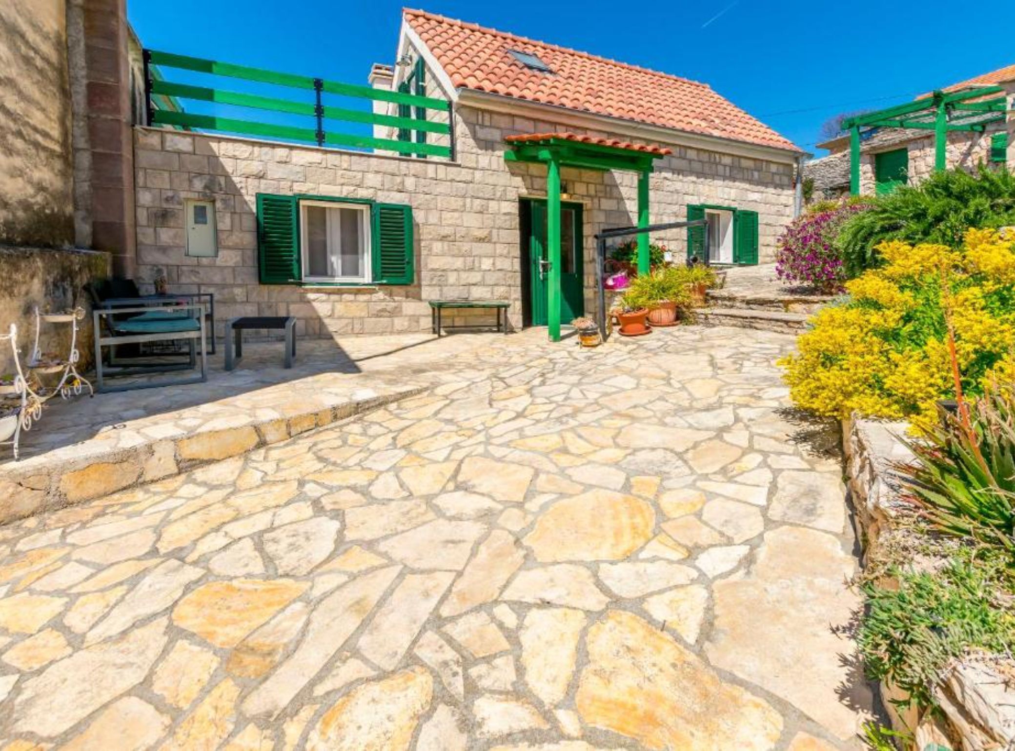 A stone building with a tiled roof, green shutters, and a stone-paved courtyard.