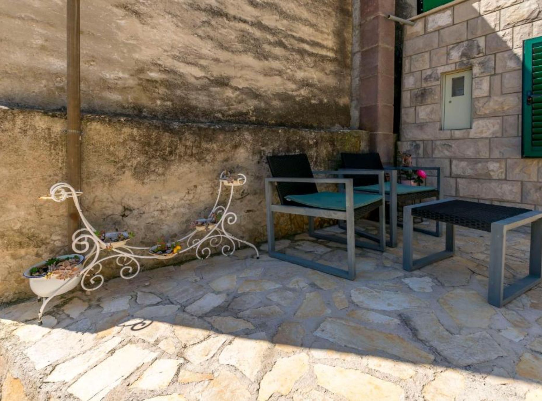 An outdoor seating area with stone flooring, metal chairs, and a table.