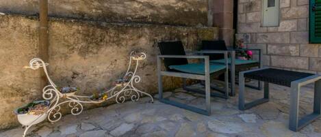 An outdoor seating area with stone flooring, metal chairs, and a table.