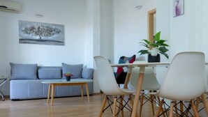 Ein modernes Wohnzimmer mit einem grauen Sofa, einem Holzesstisch mit vier Stühlen und einer Topfpflanze.